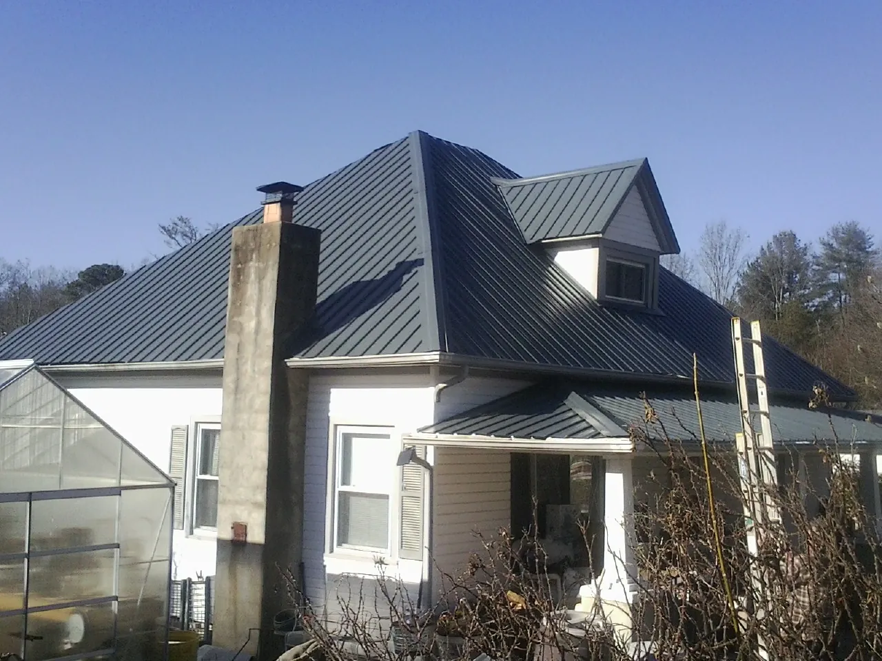 Dark blue standing seam metal roof on a white farmhouse with dormer — Slate & Tile Roof Repair by Roofing Brothers in Jakin