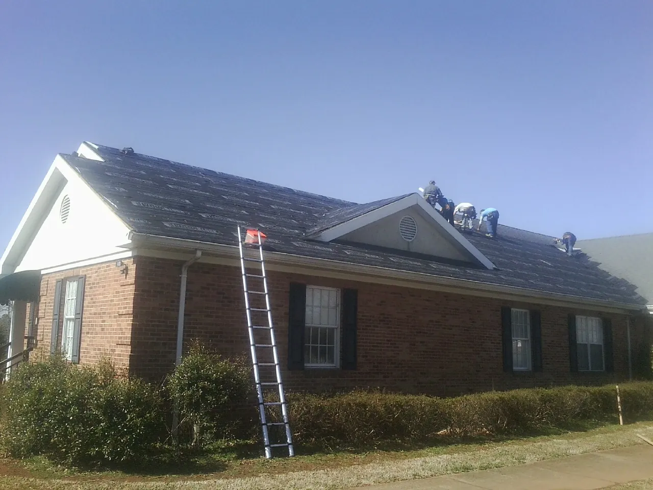 Crew tearing shingles off a brick ranch roof with a ladder set — Emergency Roof Repair work by our crew in Jakin