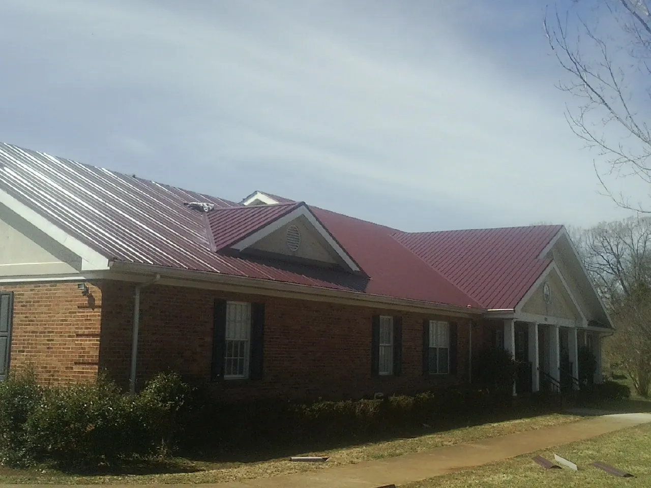 Red metal roof with gabled entries on a long brick building, from a Hail Damage Roof Repair job in Jakin