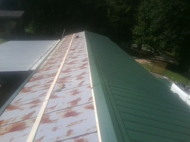 Old rusted panels beside newly installed green metal roofing — Wind Damage Roof Repair by Roofing Brothers in Jakin