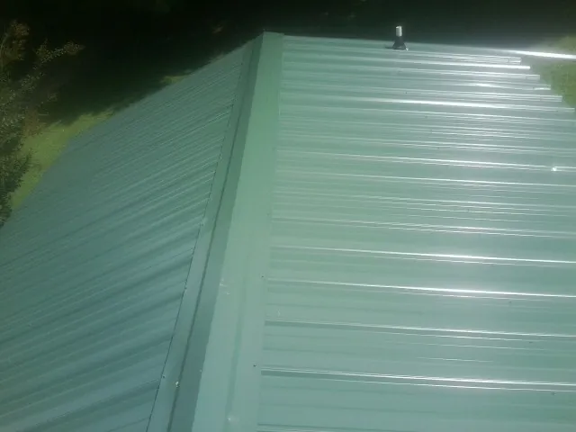 New green metal panels meeting at the ridge of a roof — Flat Roof Repair work by our crew in Jakin