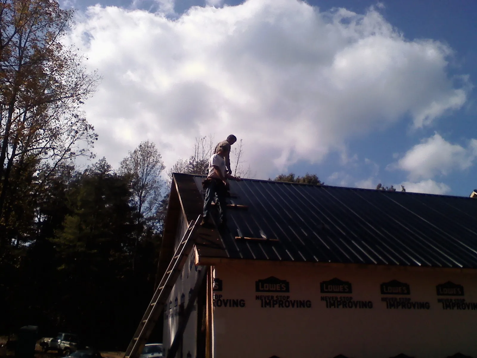 Roofer fastening dark metal panels high against a cloudy sky, from a Roof Inspection job in Jakin