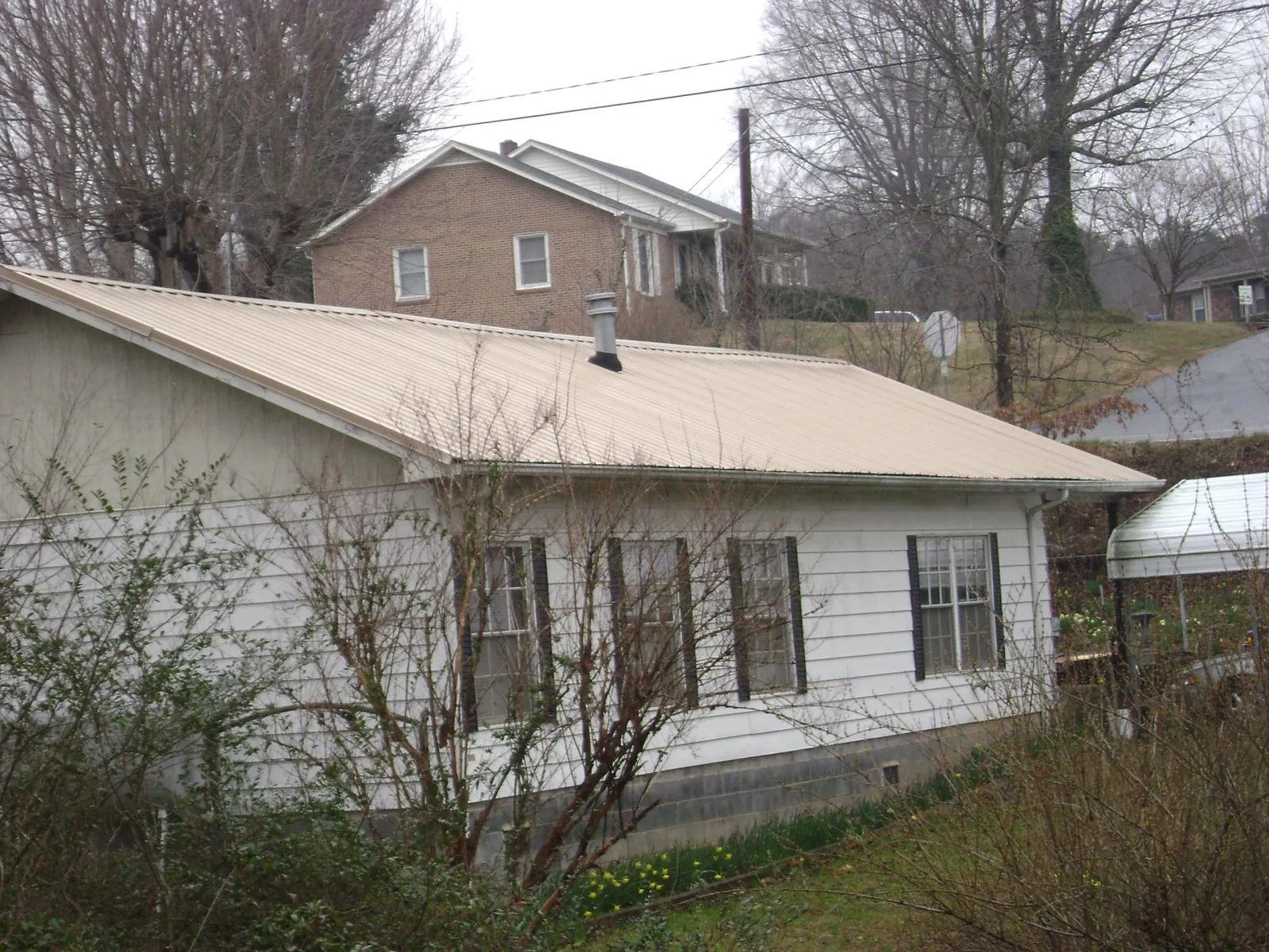 Tan metal roof on a white sided house set into a hillside — Commercial Roofing by Roofing Brothers in Jakin